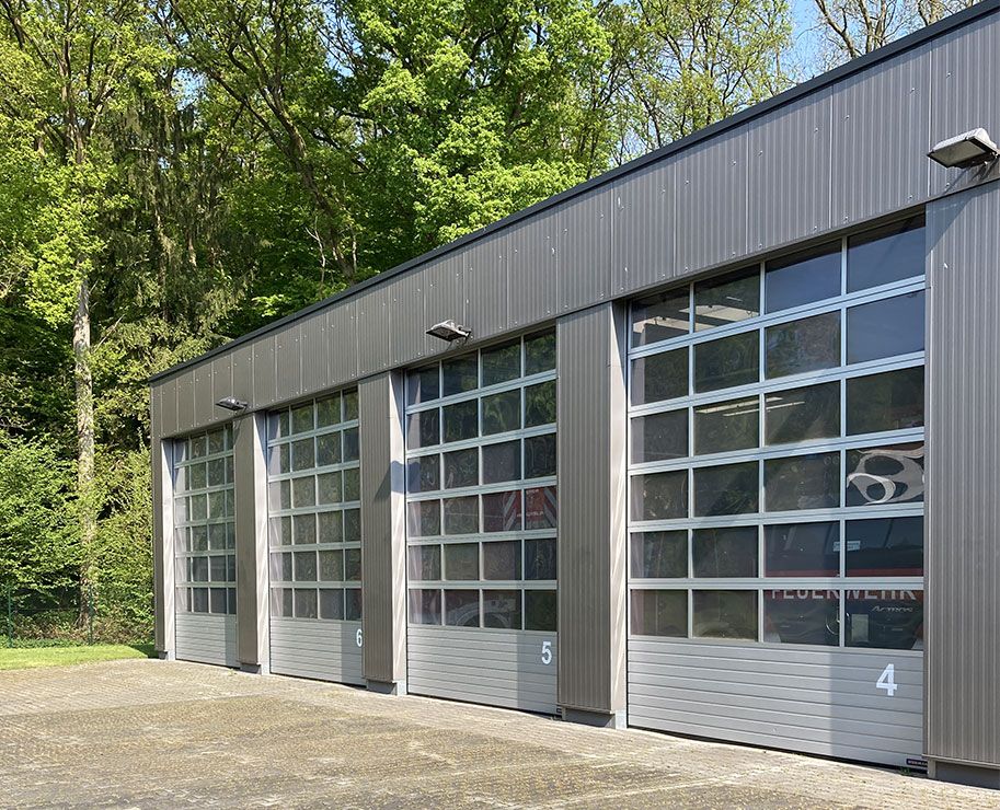 Eine große Garage mit drei großen Türen, die weit geöffnet sind und viel Platz für Fahrzeuge bietet.